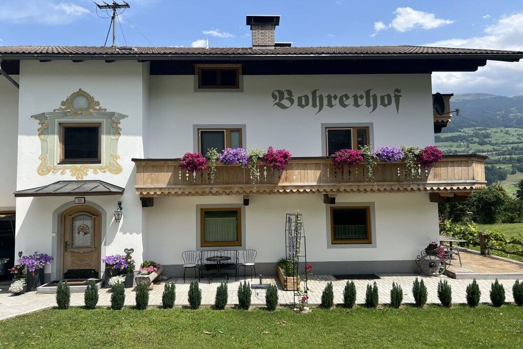 Um edifício de dois andares com uma varanda decorada com flores, uma placa com a inscrição 'Bohrechoff' e vista para o campo.