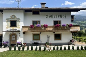 A two-story building with a balcony adorned with flowers, a sign reading 'Bohrechoff,' and a view of the countryside. - Holiday apartment with 2 bedrooms (Ried im Zillertal)