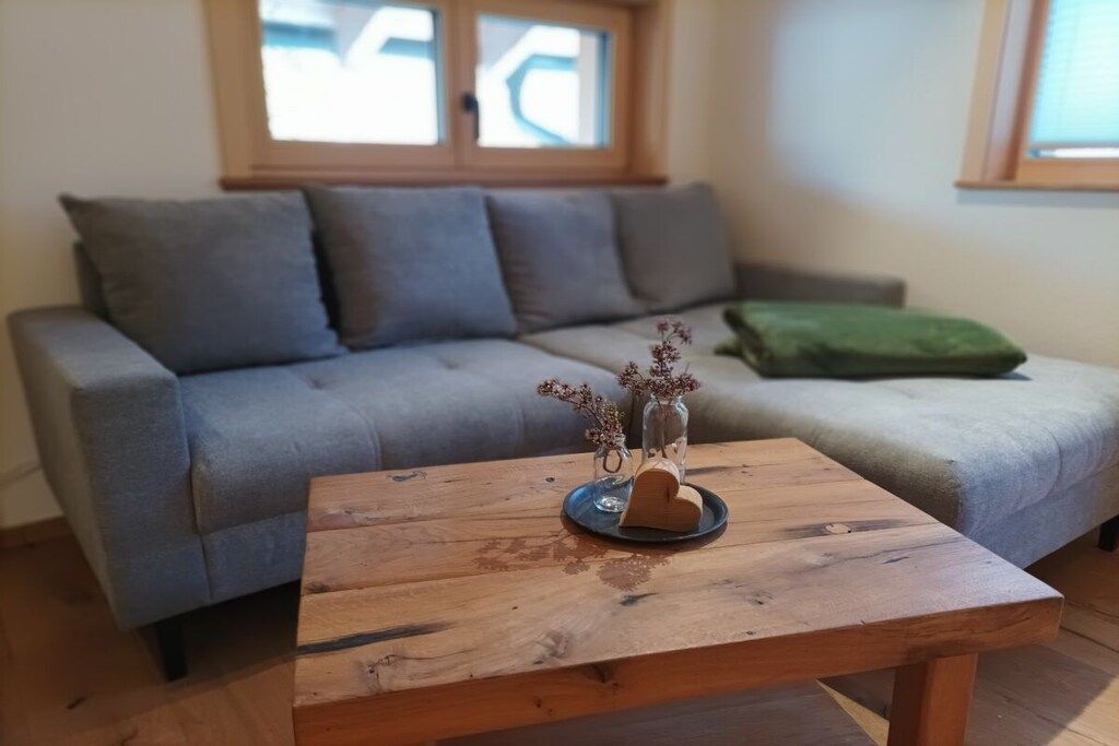 Un salon avec un canapé gris, une table basse en bois et un vase contenant des fleurs séchées.