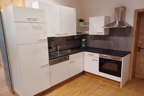 Eine kleine Küche mit weißen Schränken, einer schwarzen Arbeitsplatte, einer Edelstahl-Dunstabzugshaube und einem eingebauten Backofen.