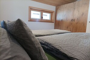 Ein Schlafzimmer mit einem Holzschrank, einem Fenster und einem Bett mit grauer Bettwäsche.
