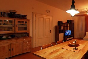 Un comedor con una mesa de madera, sillas, un mueble con puertas de cristal, un televisor y un reloj en la pared.