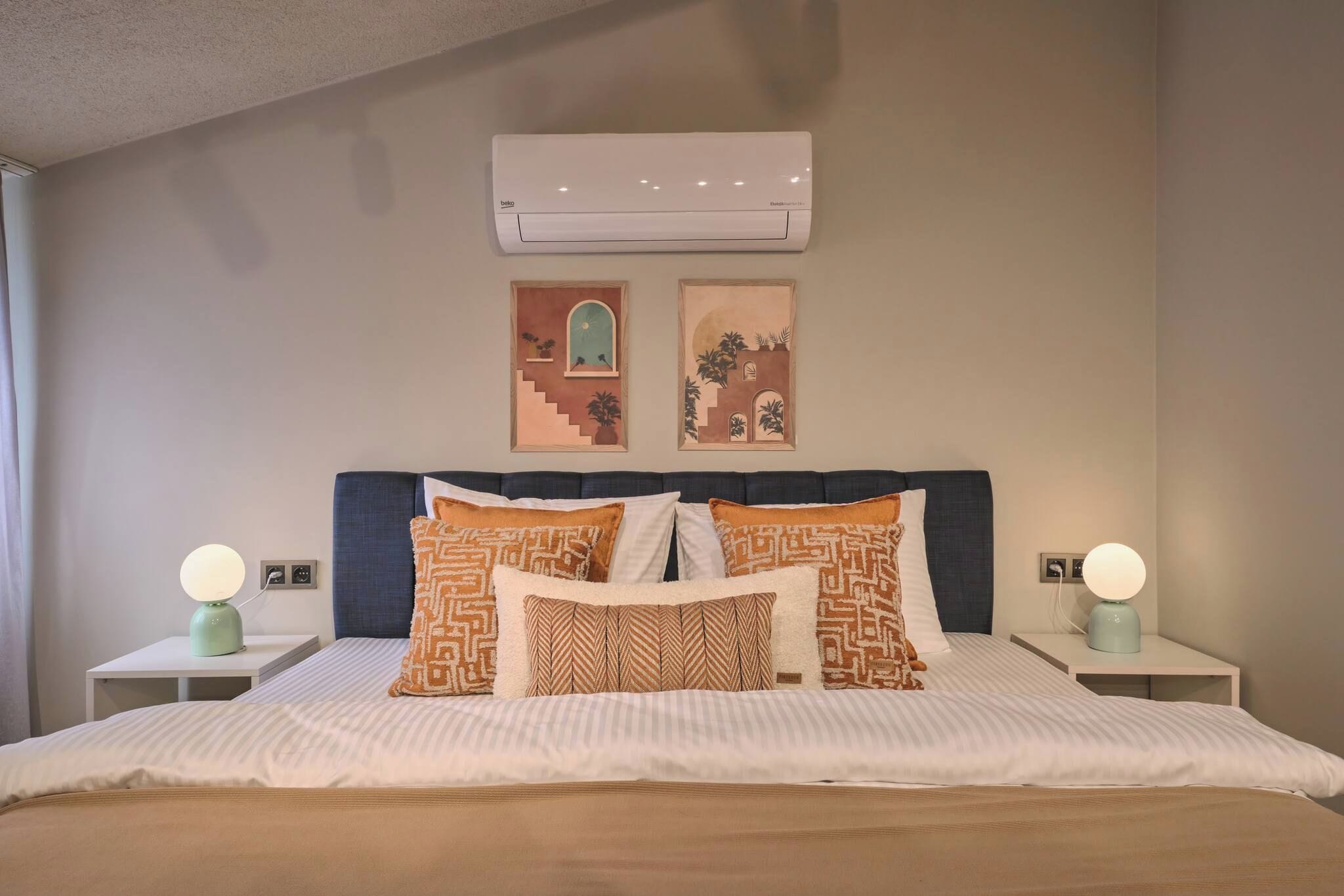 A hotel room with a bed, two bedside tables, a wall-mounted air conditioner, and two wall-mounted lamps.