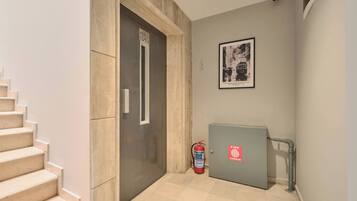 A hallway with a staircase, a fire extinguisher, and a framed picture on the wall.