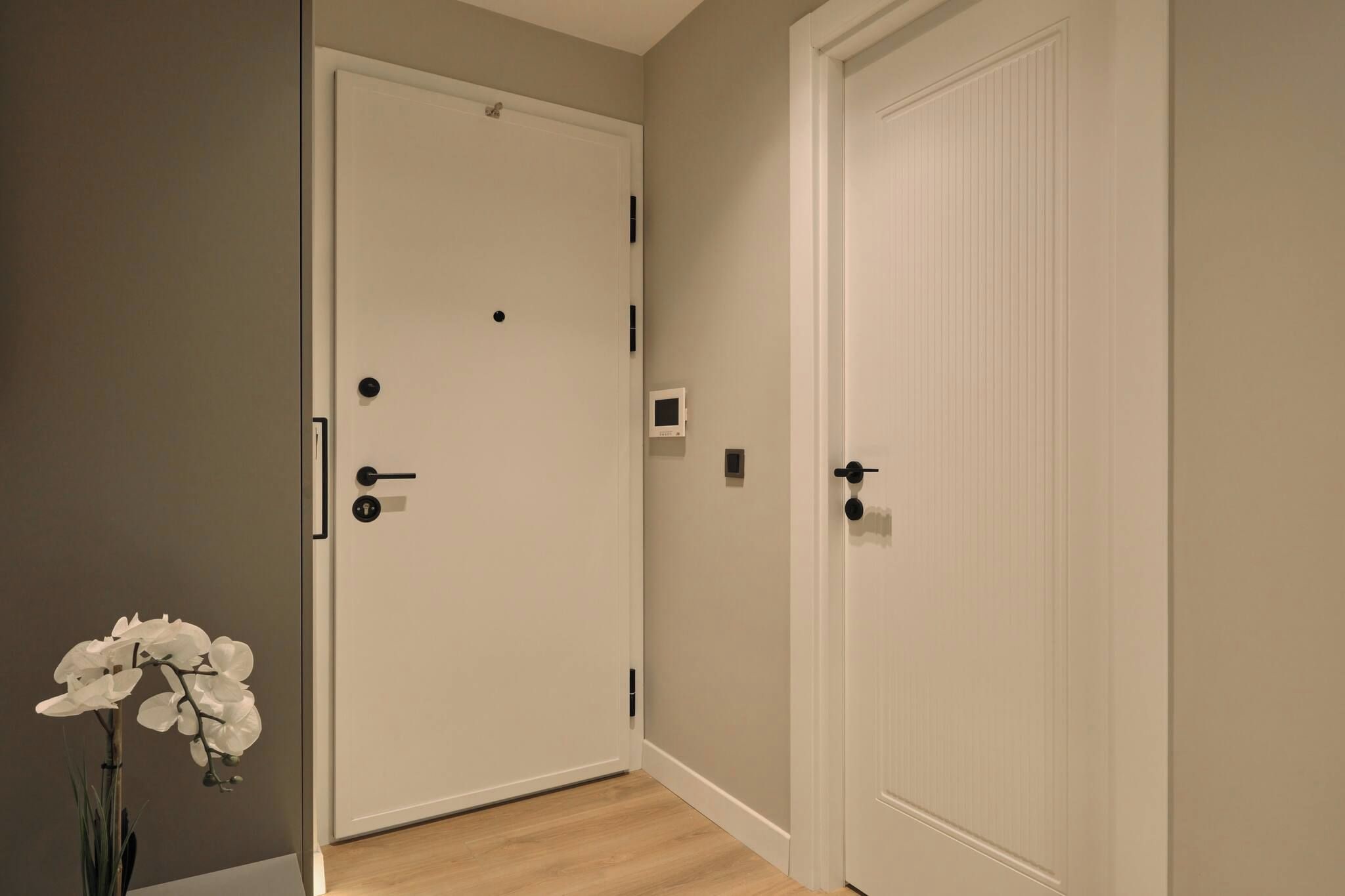 A hallway with two white doors, one with a handle and a keyhole, and another with a keyhole and a lock. There is a small window on the wall between the doors.