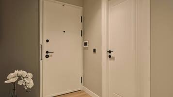 A hallway with two white doors, one with a handle and a keyhole, and another with a keyhole and a lock. There is a small window on the wall between the doors.