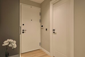 A hallway with two white doors, one with a handle and a keyhole, and another with a keyhole and a lock. There is a small window on the wall between the doors. - Polgar, 3BR, Welcoming, Charming (Kadıköy)
