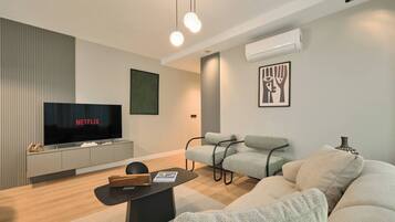 A modern living room with a flat-screen TV, grey sofas, a coffee table, and a wall-mounted air conditioner.