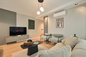 A modern living room with a flat-screen TV, grey sofas, a coffee table, and a wall-mounted air conditioner. - Polgar, 3BR, Welcoming, Charming (Kadıköy)