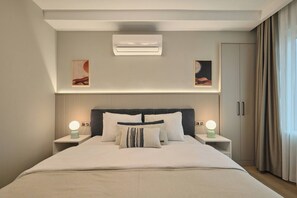 A modern hotel room with a large bed, two bedside tables with lamps, a wall-mounted air conditioner, and artwork above the bed. - Polgar, 3BR, Welcoming, Charming (Kadıköy)