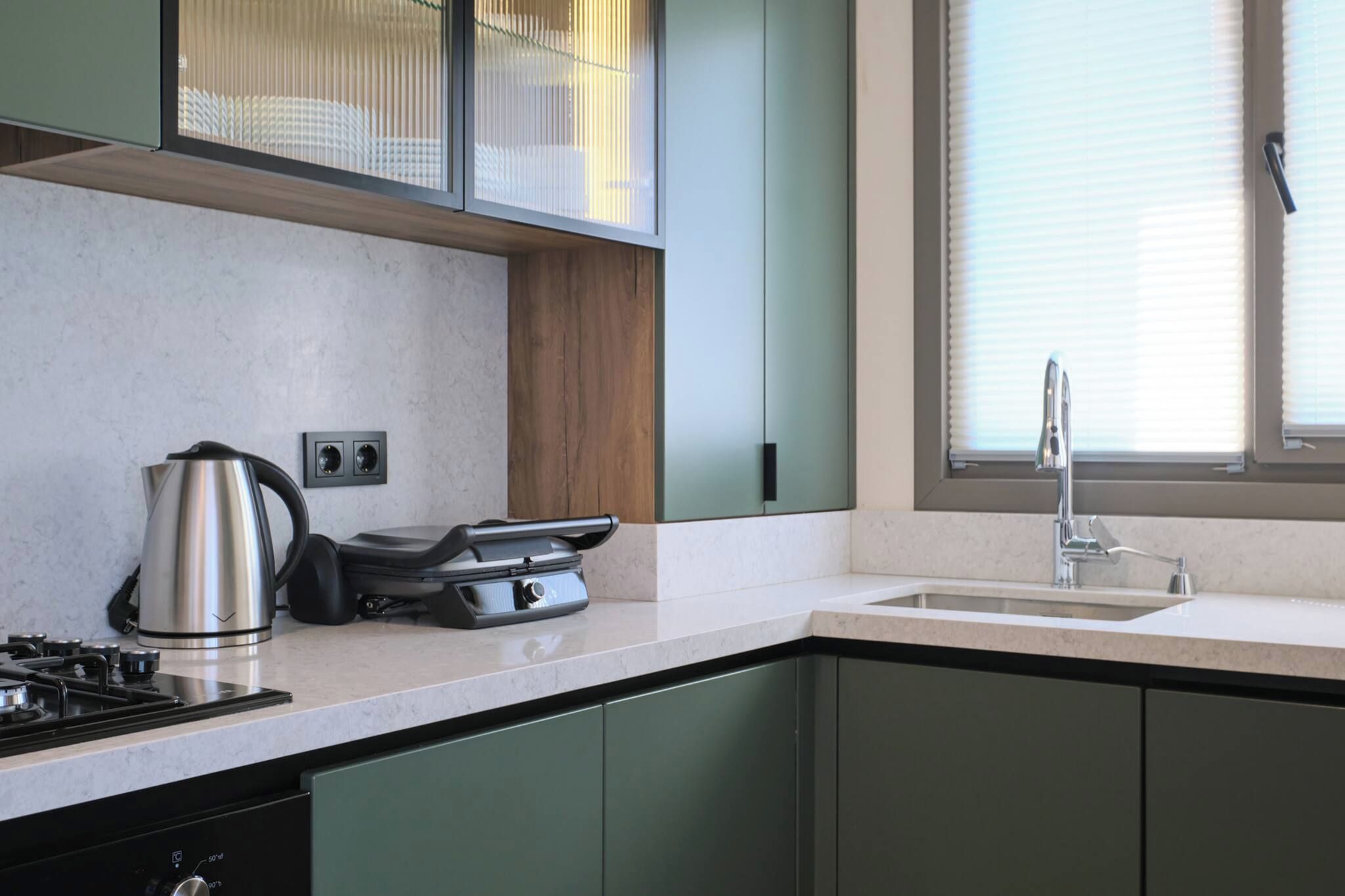 A modern kitchen with a gas stove, a kettle, a toaster, and a sink with a faucet.