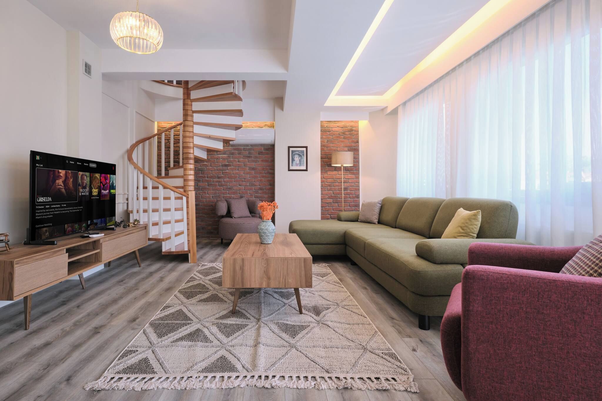Ein modernes Wohnzimmer mit einer Holztreppe, einem Flachbildfernseher, einem grünen Sofa und einem gemusterten Teppich.