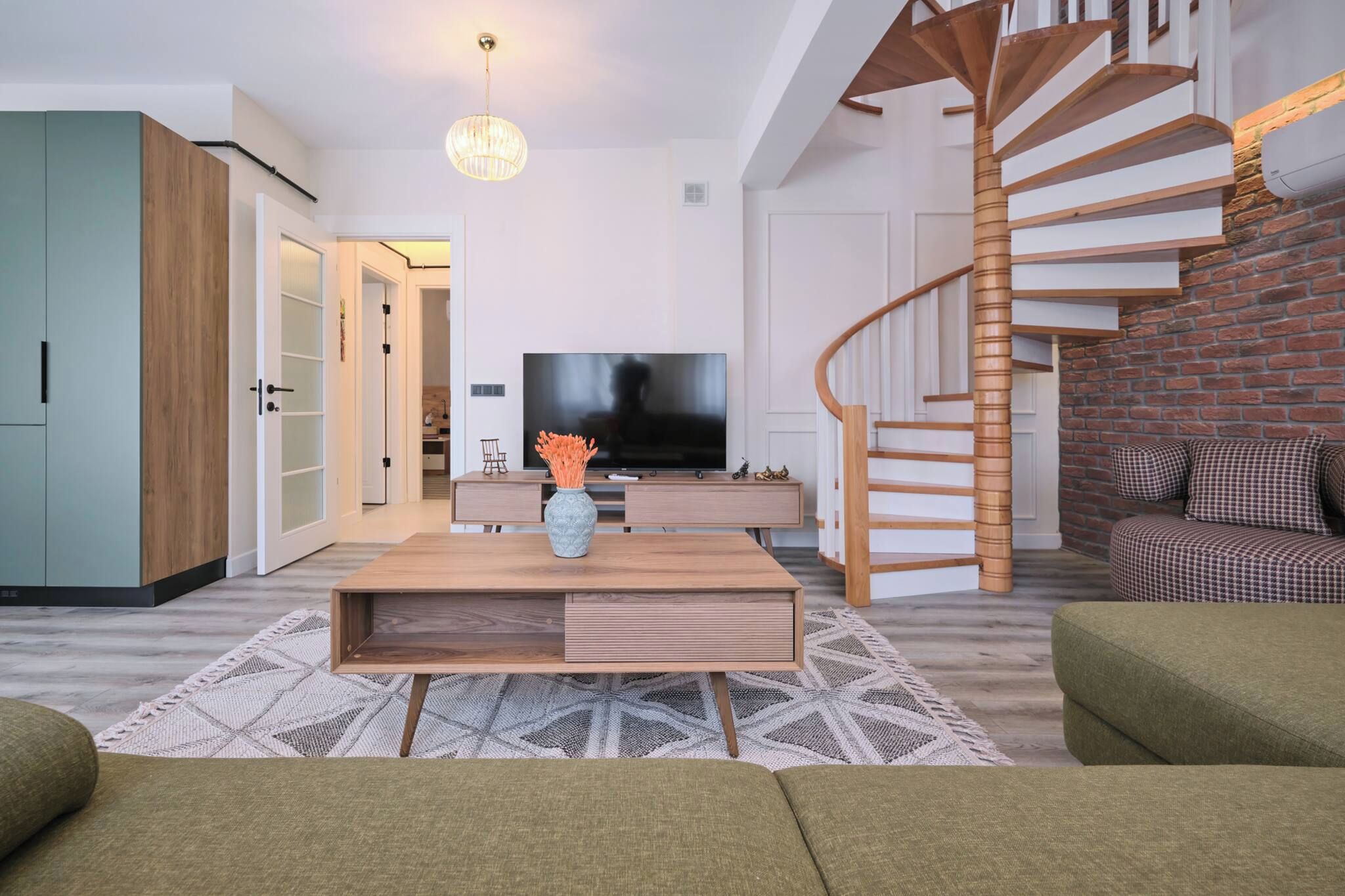 A modern living room with a wooden coffee table, a flat-screen TV, a staircase, and a sofa.