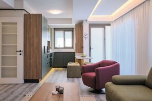 Ein modernes Wohnzimmer mit Couchtisch aus Holz, zwei Sesseln, einer Küchenzeile mit Fenster und einer Schiebetür.