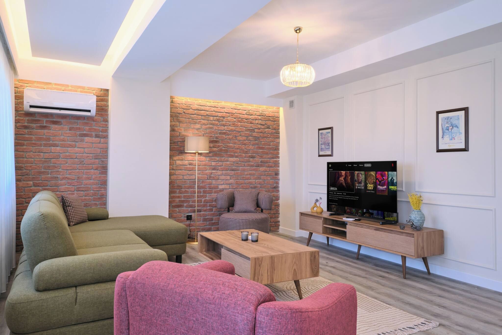 Een moderne woonkamer met een bank, fauteuil, salontafel en een televisie op een houten standaard.