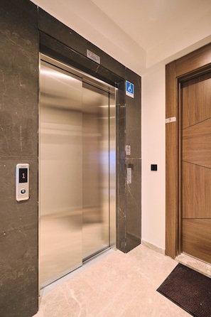 Ein Hotelaufzug mit digitaler Anzeige, einem Rollstuhlzugang-Schild und einer Holztür.