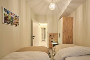 A bedroom with two beds, a wooden wardrobe, a hanging light fixture, and a wall-mounted picture. - Cassiopeia, 2BR, Sea View Balcony Best Loc (Kadıköy)