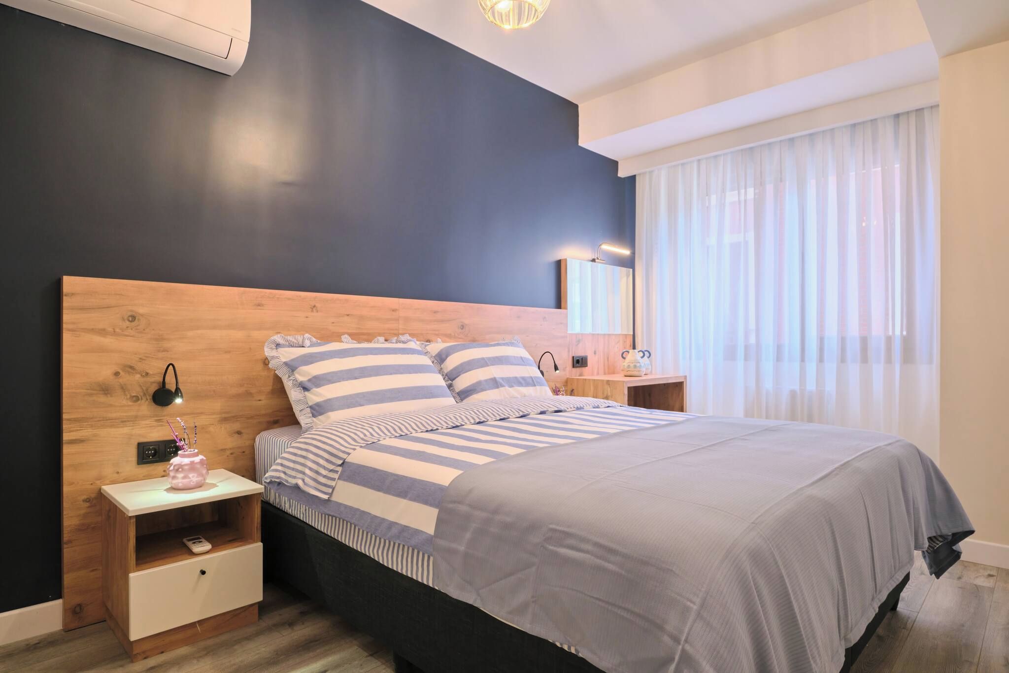 Une chambre à coucher moderne avec un grand lit, une tête de lit en bois, des tables de chevet et une petite table de nuit avec une lampe.