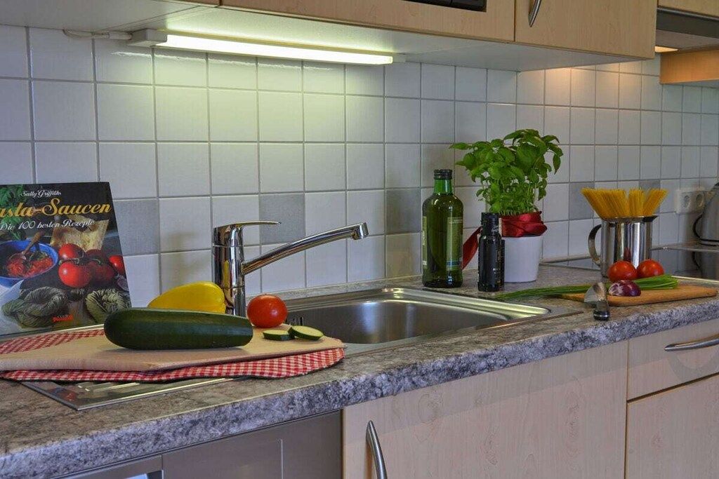 A kitchen with a sink, a cutting board with vegetables, a book, and a potted plant.