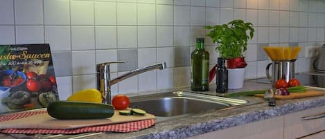 A kitchen with a sink, a cutting board with vegetables, a book, and a potted plant.