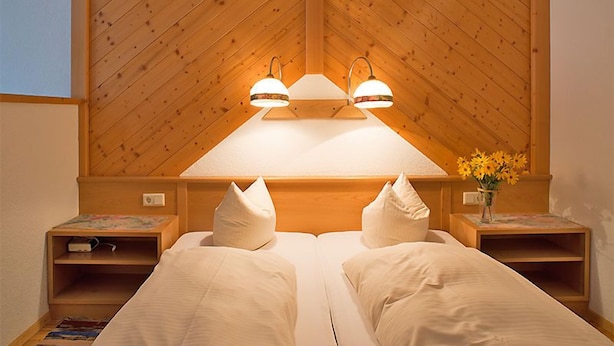 Een tweepersoonsbed met twee kussens, een houten hoofdbord, nachtkastjes en een vaas met bloemen.