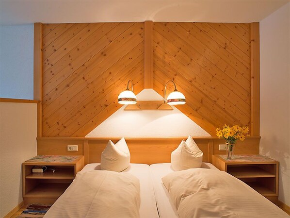 Uma cama de casal com duas almofadas, cabeceira de madeira, mesas de cabeceira e um vaso com flores.