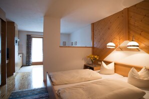 Quarto com cabeceira de madeira, duas camas, mesa de cabeceira com um vaso de flores e vista para a cozinha.