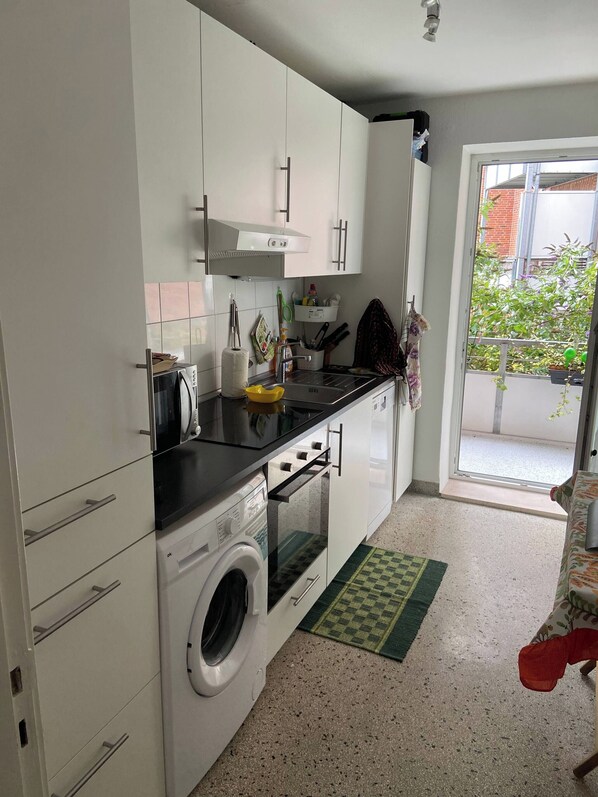 A compact kitchen with white cabinets, a washing machine, and a small oven.