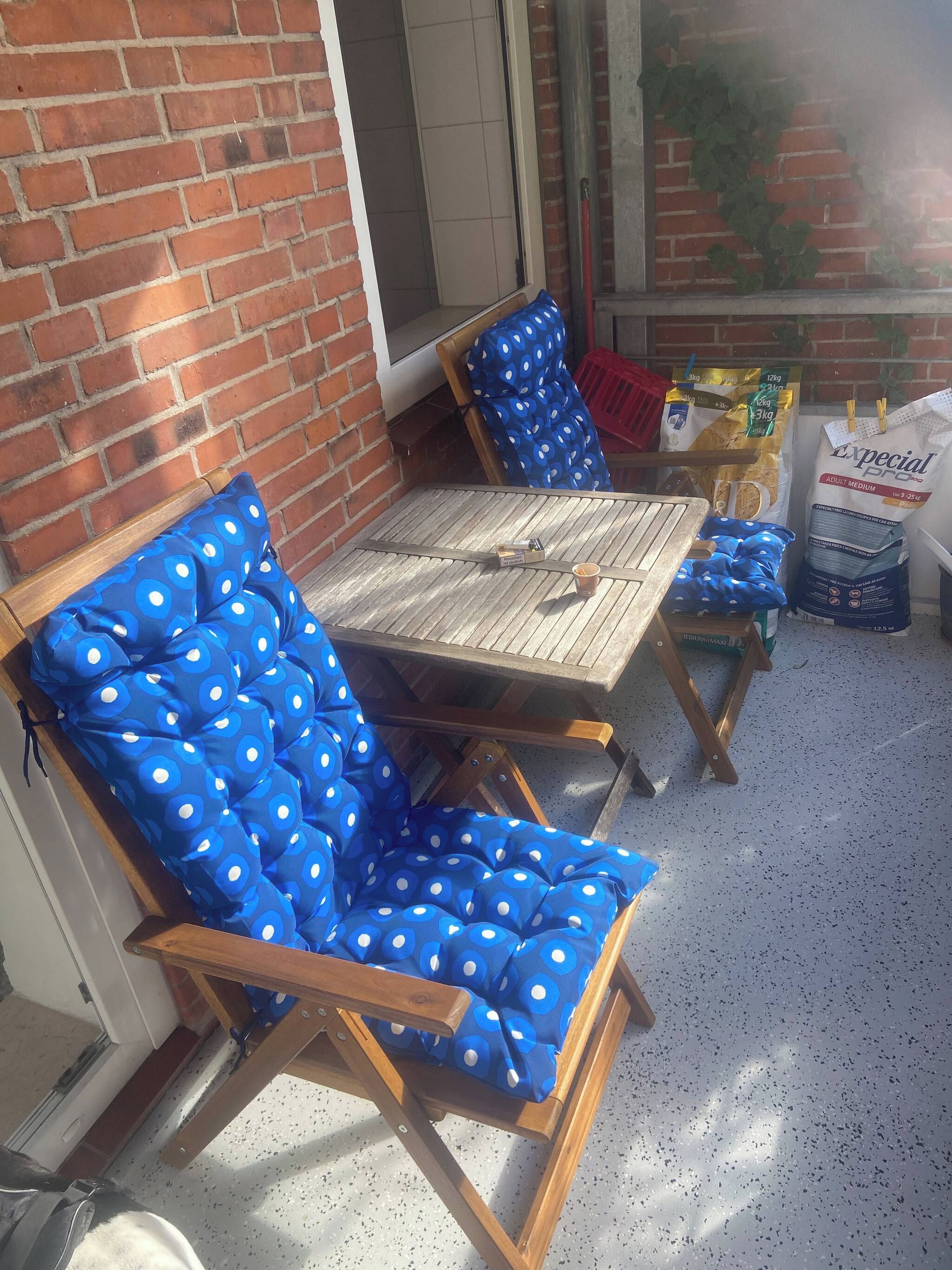 A patio area with a brick wall, a wooden table, and blue polka-dotted chairs.
