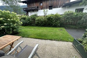 Una terraza de madera con una mesa y sillas, un patio con césped y un edificio con balcón.