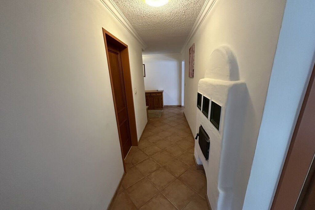A narrow hallway with a wooden door on the left and a white wall with a black object on the right.