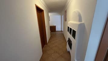 A narrow hallway with a wooden door on the left and a white wall with a black object on the right.
