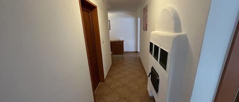 A narrow hallway with a wooden door on the left and a white wall with a black object on the right.