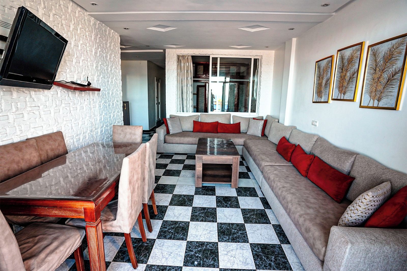 Een woonkamer met een bank, stoelen, een salontafel, een aan de muur bevestigde televisie en een geruit vloerkleed.