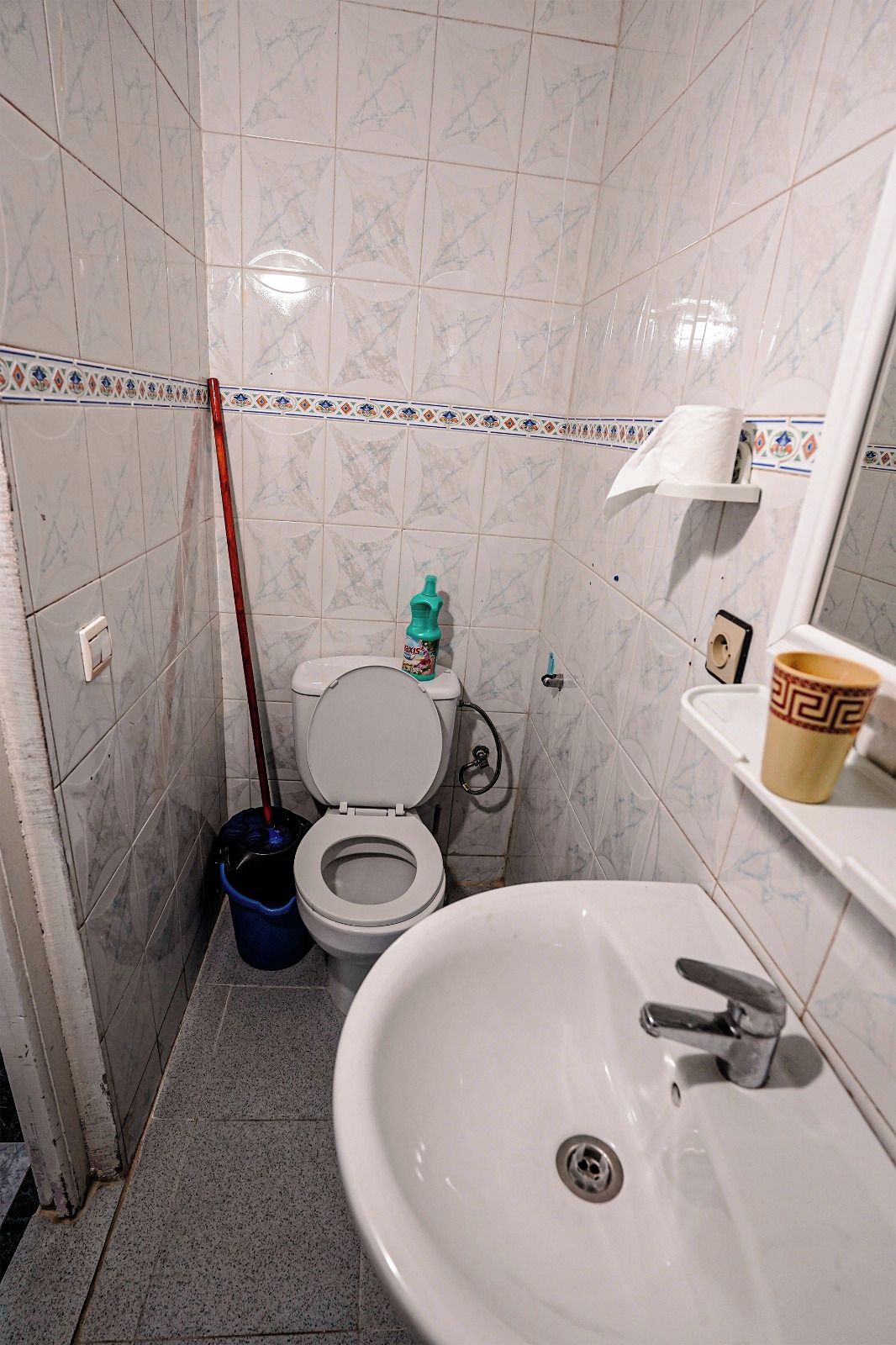 Un baño con inodoro, lavamanos y escoba.