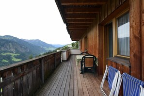 Um deck de madeira com mesa e cadeiras, com vista para uma paisagem montanhosa.