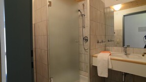 Un baño moderno con cabina de ducha de vidrio, lavamanos con espejo y techo de madera.