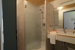 Uma casa de banho moderna com cabine de chuveiro em vidro, uma pia com espelho e teto de madeira.