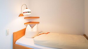 Una cama individual con cabecera de madera, una lámpara de noche y una almohada.