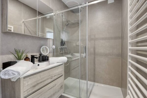 A modern bathroom with a glass shower enclosure, a wooden vanity with a towel, and a mirror.