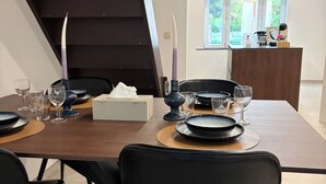Et moderne spiseområde med et træbord dækket til fire personer, sorte stole og en trappe i baggrunden.