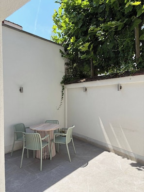 A patio with a table and chairs, a white wall, and a tree with green leaves.