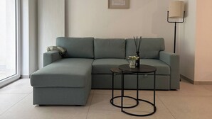 En moderne stue med en grå hjørnesofa, et lille rundt bord med en vase og stearinlys, en gulvlampe og et indrammet billede på væggen.