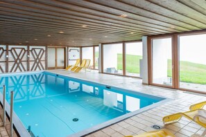 A swimming pool with clear glass walls, yellow lounge chairs, and a view of the outdoors. - Top 9 for 2-3 people / 1st floor (Schröcken)