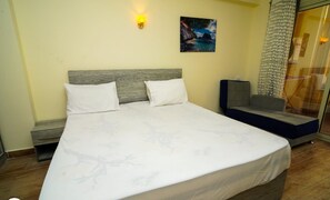 Ein ordentlich bezogenes Bett mit weißen Leinen und Kissen, ein Holz-Kopfteil und ein Gemälde mit einer Küstenansicht an der Wand.