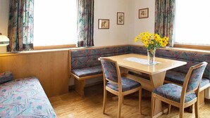 Una habitación acogedora con una mesa de madera, cuatro sillas, un banco y una ventana con cortinas.