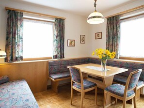 Um quarto aconchegante com uma mesa de madeira, quatro cadeiras, um banco e uma janela com cortinas.
