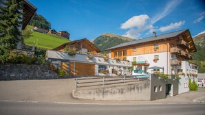 Un hotel con fachada de madera, un letrero de restaurante a la vista y montañas al fondo.