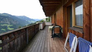Terraza de madera con mesa y sillas, con vistas a un paisaje montañoso.