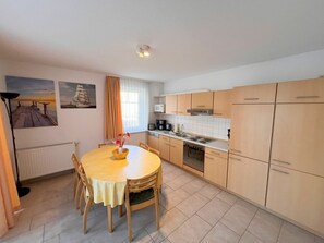 A compact kitchen with a dining table, chairs, and basic appliances. - Ground Floor 05 Holiday Apartment at Wilhelmsberg (Heringsdorf)